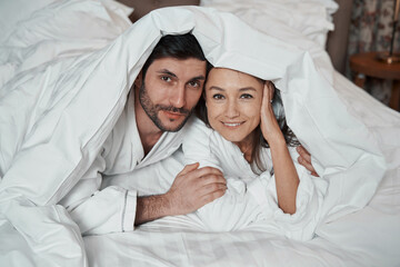 Woman and her partner staring at camera from under blanket