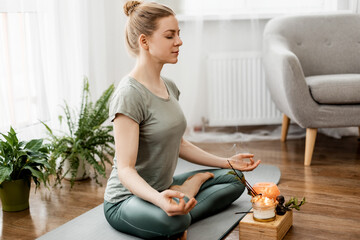 Beautiful happy girl with closed eyes practicing yoga in lotus position in bedroom in the morning