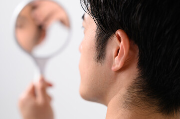 Obraz premium 手鏡で顔をチェックする男性 メンズ美容