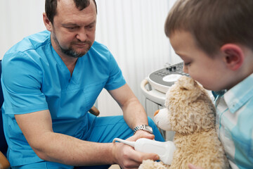 Caring medical worker examining the boy and his teddy bear