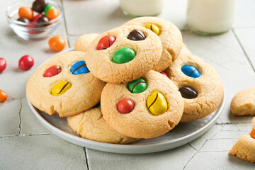 Homemade cookies with colorful chocolate candies and milk. Stack of shortbread cookies with multi colored candy on plate with bottle of milk on light gray background. Baby food concept. Copy space.