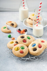 Homemade cookies with colorful chocolate candies and milk. Stack of shortbread cookies with multi colored candy on plate with bottle of milk on light gray background. Baby food concept. Copy space.