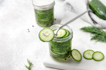 Slice of cucumber on fork with glass jar with Marinated cucumbers. Vegetable snack, copy space