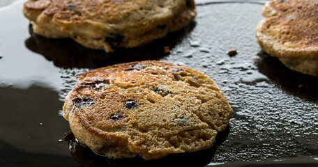 Blueberry pancakes frying on a cast iron griddle pan.
