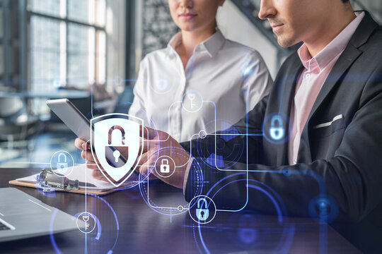 Businessman and businesswoman working together to protect clients confidential information and cyber security. IT hologram padlock icons over office background with panoramic windows.