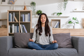 Clam of Asian young woman doing yoga lotus pose to meditation and relax on couch during work online at home.Happiness female break after worked close her eyes and deep breath with yoga so peaceful. - obrazy, fototapety, plakaty