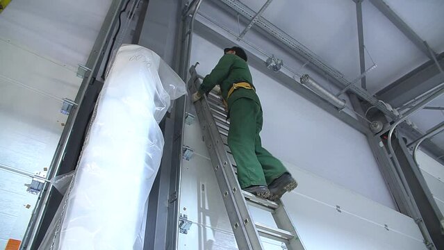 Professional worker climbing up ladder indoors to repair a transformer. Man in a workwear