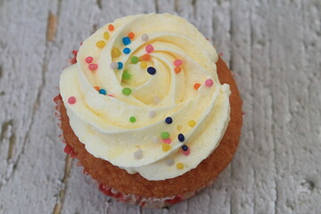 Sweet cake with tutti frutti sprinkles on top on the wooden table white background.
