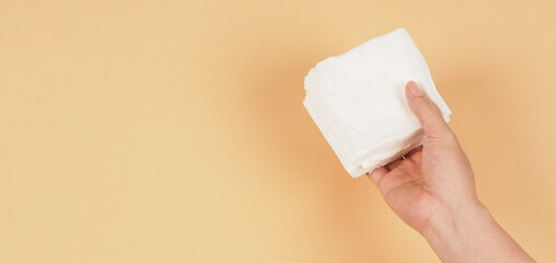 The hand is  holding a small size of white paper tissues on a creamy ivory color background.