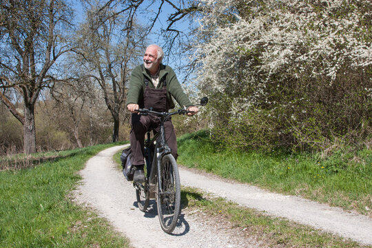 Elderly man rides his bike on a dirt road, past blooming sloe bushes and is happy about the wonderful spring day in difficult times.