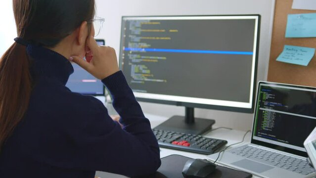 Young Asian woman, developer programmer, software engineer, IT support, wearing glasses working on computer to check coding in bugging system. Back view