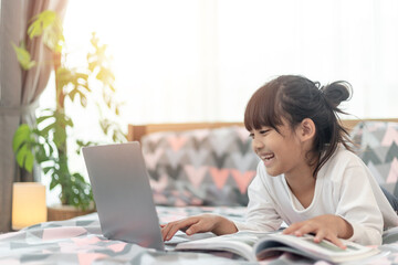 Little Asian girl using a laptop while lying on the bed