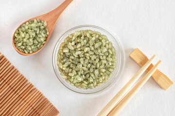 Green rice in a glass bowl with Chinese chopsticks and a spoon of rice