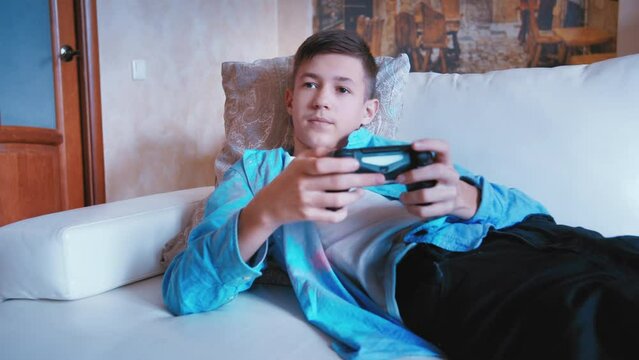 cinematic of teen boy sitting on the sofa and plays a game on a console
