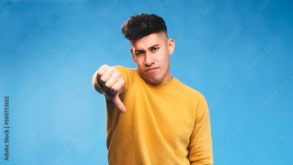 Poster man showing thumb down at camera while standing on an isolated background.