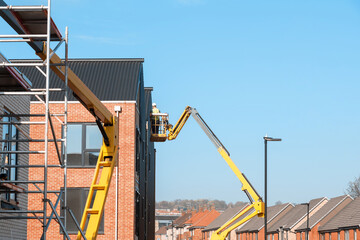 Builders working off Telescopic Boom Lift while fitting insulated sandwich panels to the facade of...