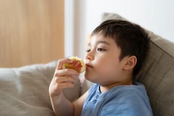 Healthy child eating red apple, Cute boy eating fresh fruit for his snack while watching TV in living room, Close up kid face eating food. Healthy food for children concept