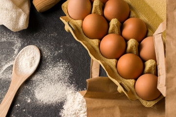 Natural fresh chicken eggs in eco package, flour on a dark kitchen table, linen towel. Traditional ingredients for baking. Top view. Flat lay. Kinfolk style.