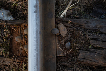 railway rail top view with rusty fasteners hammered into a wooden ruined beam around dry grass with remnants of fuel oil