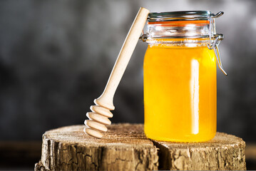 Honey jar and dripper on  tree stump. grey background.