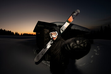 Fototapeta na wymiar portrait of young man in a black winter suit and ski goggles with skis on his shoulder