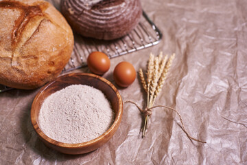 whole grain flour, eggs and two types of freshly baked round bread. homemade bread with a sprig of tied ears. food background