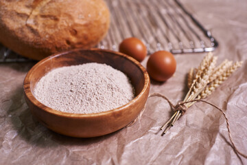 whole grain flour closeup, eggs and freshly baked round bread. homemade bread with a sprig of tied ears. food background