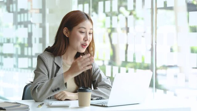 Business woman video calling greeting customers at office desk from laptop computer.