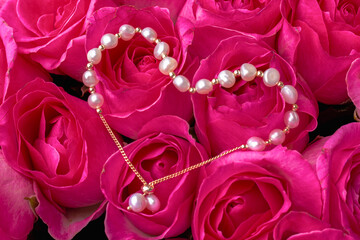 A string of pearls lies on the buds of pink roses