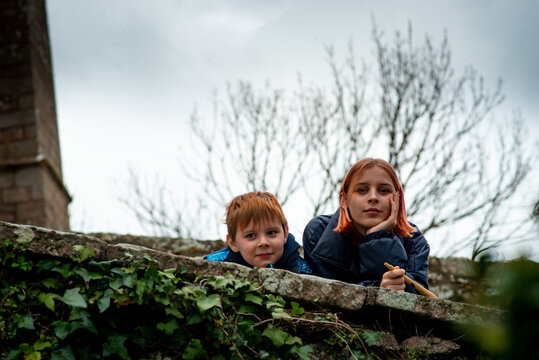 brother and sister stand leaning against the parapet in the spring