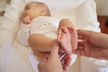 female hands hold the small legs of a newborn baby who lies in the crib