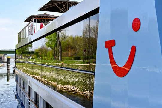 Breisach, Germany - April 2022: Close up view of the TUI logo on the side of a river cruise ship with the riverbank reflected in the boat's windows