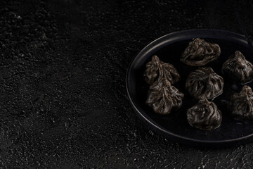 Traditional Georgian dish, khinkali Kalakuri, black dumplings stuffed with minced meat on black plate on black textured background