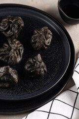 Traditional Georgian dish, khinkali Kalakuri, black dumplings stuffed with minced meat on black plate on beige colored background