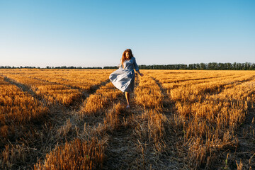 Naklejka na ściany i meble Woman in blue linen dress enjoying nature in sunset field. Stress and psychological resilience. Spend Time in Nature to Reduce Stress and Anxiety.