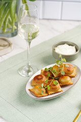 Deep fried traditional italian dish - ravioli, dumplings stuffed with minced meat, oregano branch, sour cream, a glass with champagne on green table cloth