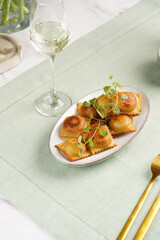 Deep fried traditional italian dish - ravioli, dumplings stuffed with minced meat, oregano branch, sour cream, a glass with champagne on green table cloth