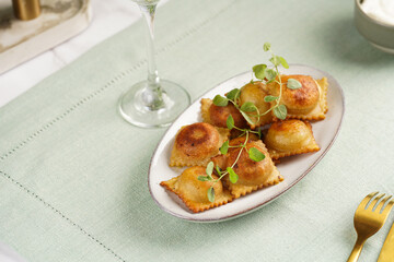 Deep fried traditional italian dish - ravioli, dumplings stuffed with minced meat, oregano branch, sour cream, a glass with champagne on green table cloth