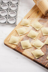Freshly made traditional italian dish - ravioli, dumplings stuffed with minced meat, on wooden board with flour, aluminum form for preparation
