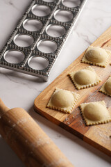 Freshly made traditional italian dish - ravioli, dumplings stuffed with minced meat, on wooden board with flour, aluminum form for preparation