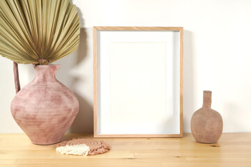 Scandinavian Boho Theme Product Mockup. Empty vertical frame with modern beige ceramic vases with dried palm frond leaf against a white wall background.