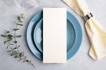 Vertical menu card mockup with festive wedding or birthday table setting, eucalyptus, blue ceramic plate on grey background. Empty blank card mock up. Restaurant menu concept. Flat lay, top view