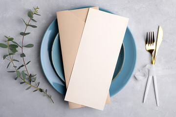 Vertical menu card mockup with festive wedding or birthday table setting with golden cutlery, eucalyptus, blue ceramic plate on grey background. Restaurant menu concept. Flat lay, top view