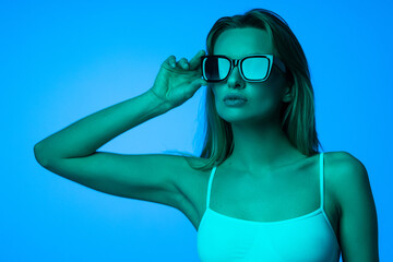 Fashion portrait of beautiful woman face with sunglasses on blue light color.