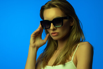 Fashion portrait of beautiful woman face with sunglasses on blue light color.