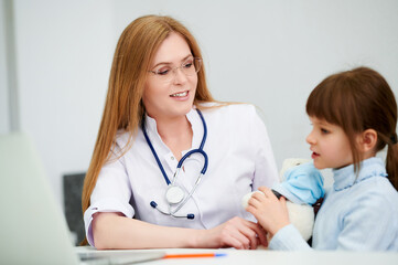Female caucasian doctor with little girl patient and teddy bear toy in office hospital