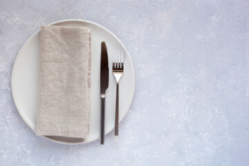 White plate with cutlery and linen napkin on the grey concrete background