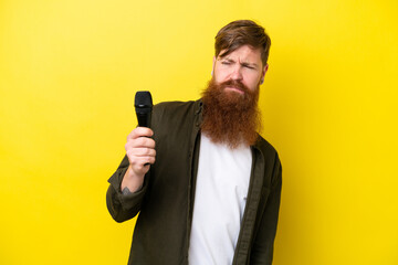 Naklejka premium Redhead man with beard picking up a microphone isolated on yellow background with sad expression