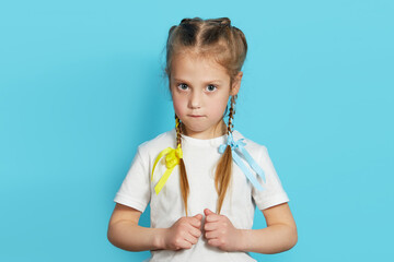 Portrait of a sad little patriot girl with multi-colored bows in pigtails on a blue background....