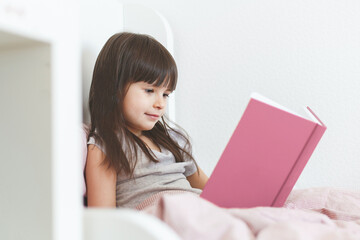 one todder girl 5 years old brunette with long hair sits in bed and reads a book
